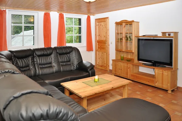 Wohnzimmer mit dunkler Sitzgruppe, Couchtisch, Fenster und Holzschrank.