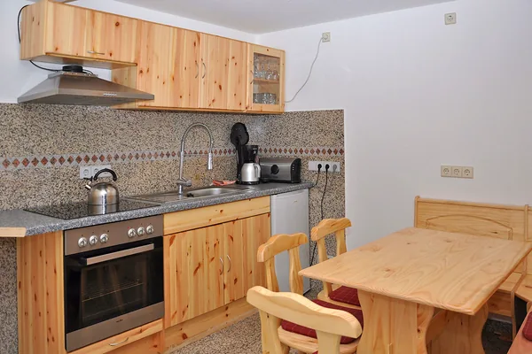 Küche mit Holzfronten, Herd, Spüle und kleinem Esstisch.