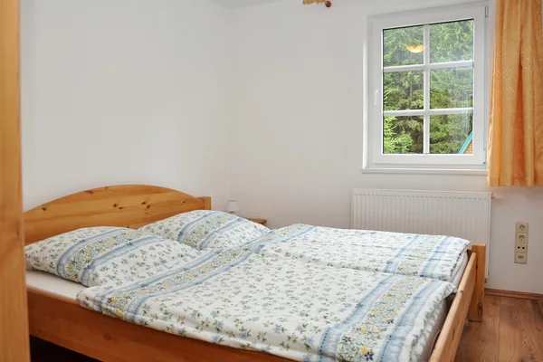 Schlafzimmer mit Doppelbett, Holzbettrahmen und Fenster.