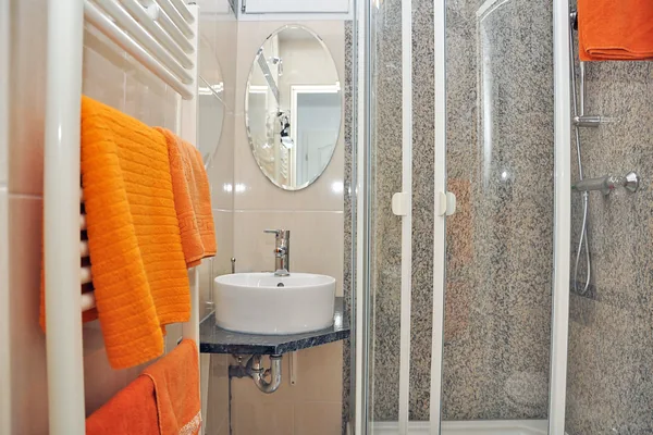 Duschbad mit Waschbecken, Spiegel, Dusche und orangefarbenem Handtuch.