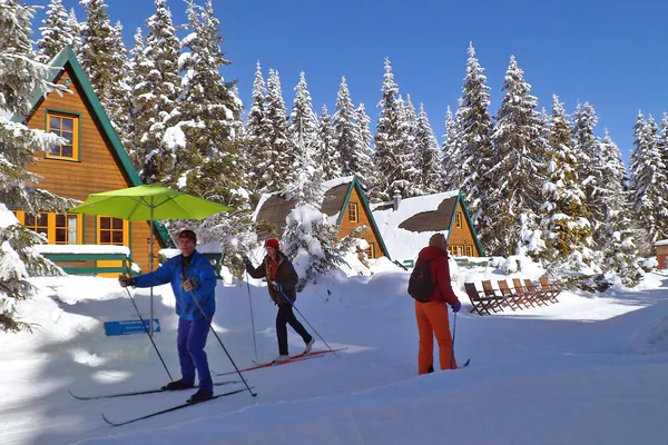 Schneebedeckte Finnhütten und Menschen mit Langlaufskiern.