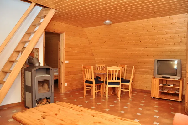Wohnraum einer Finnhütte mit Kaminofen, Esstisch und Holztreppe.