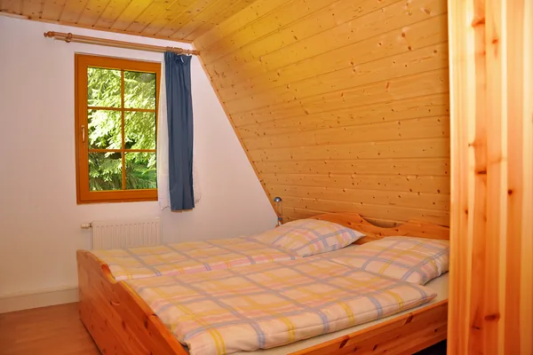 Schlafzimmer einer Finnhütte mit Doppelbett, Fenster und Dachschräge.