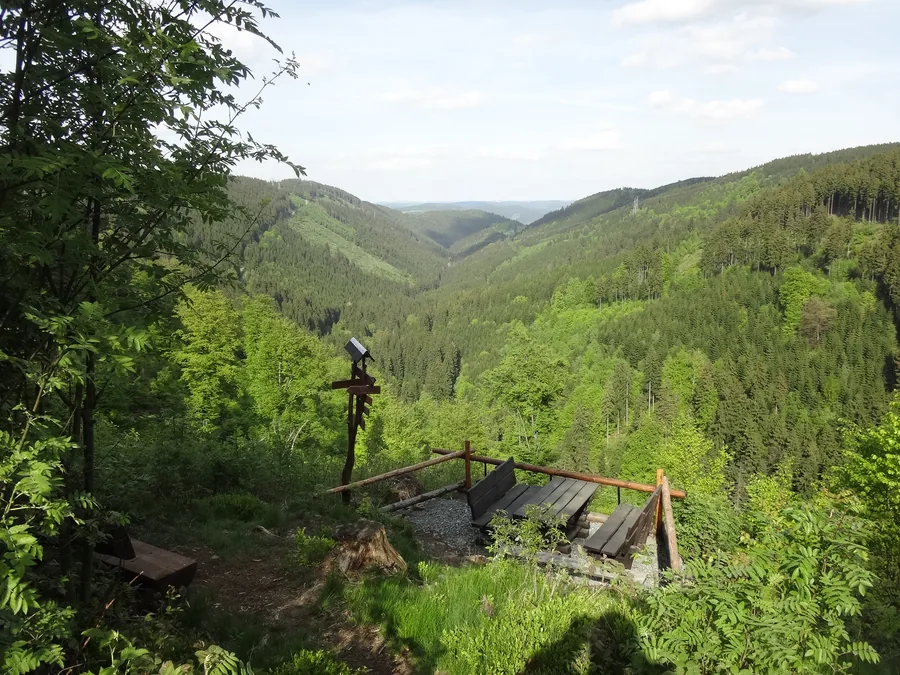 Hölzerner Sitzplatz vor einem weiten Tal mit dicht bewaldeten Hängen.
